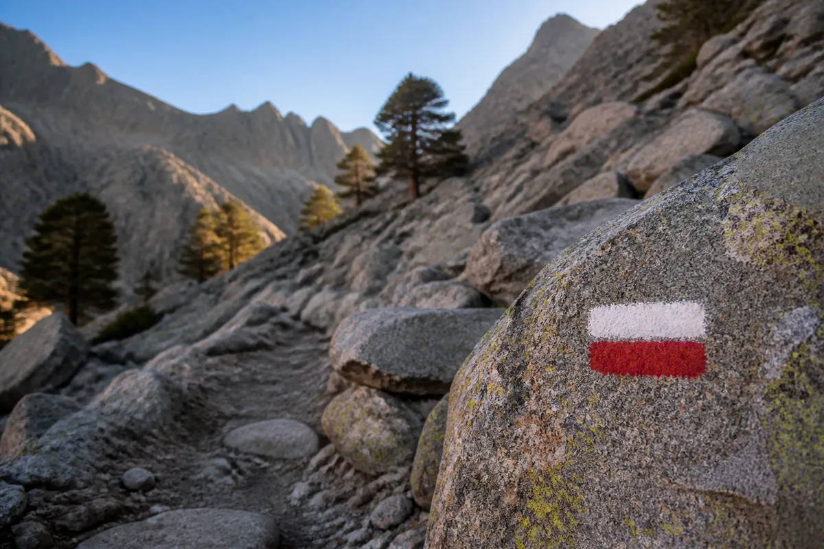Sentier rocheux balisé de blanc et de rouge serpentant sur une crête corse au lever du soleil