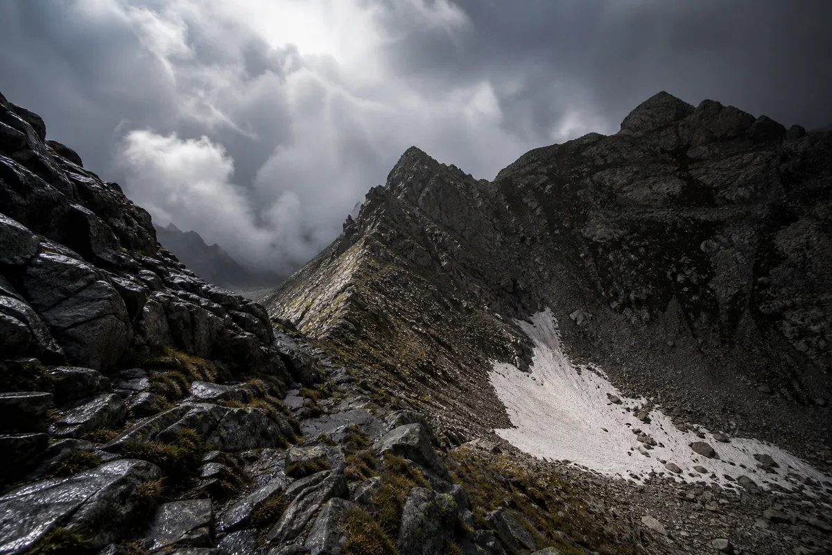 Névé résiduel accroché à un col rocheux corse sous un ciel chargé de nuages d’orage