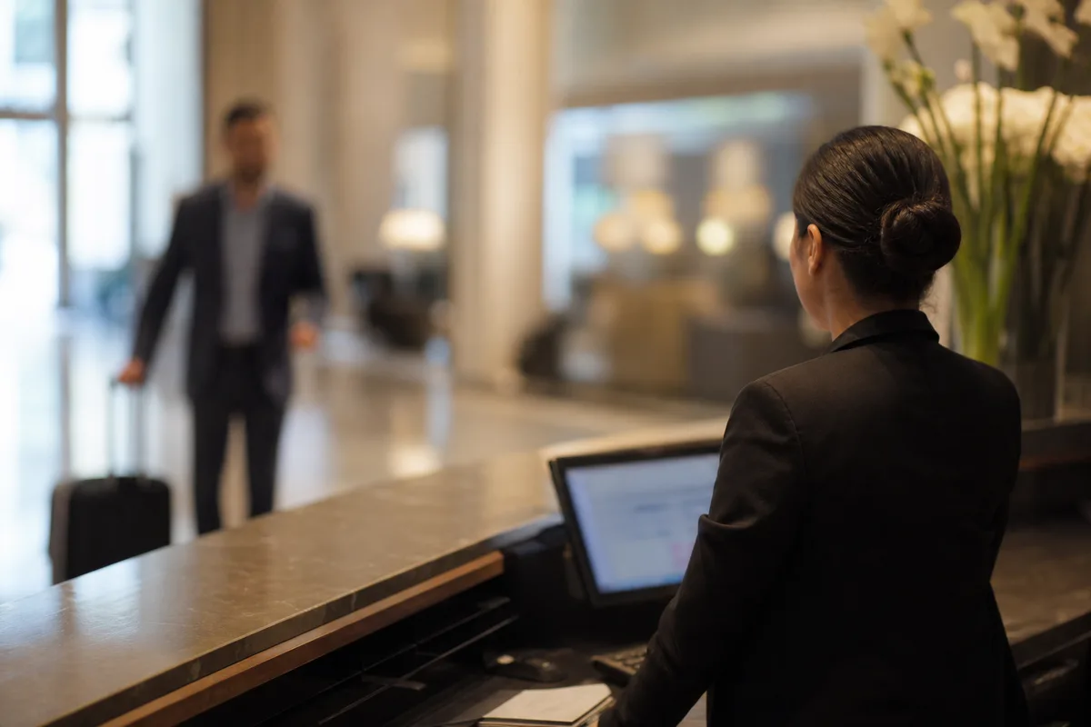 Réceptionniste d’hôtel de dos accueillant un client dans un lobby moderne