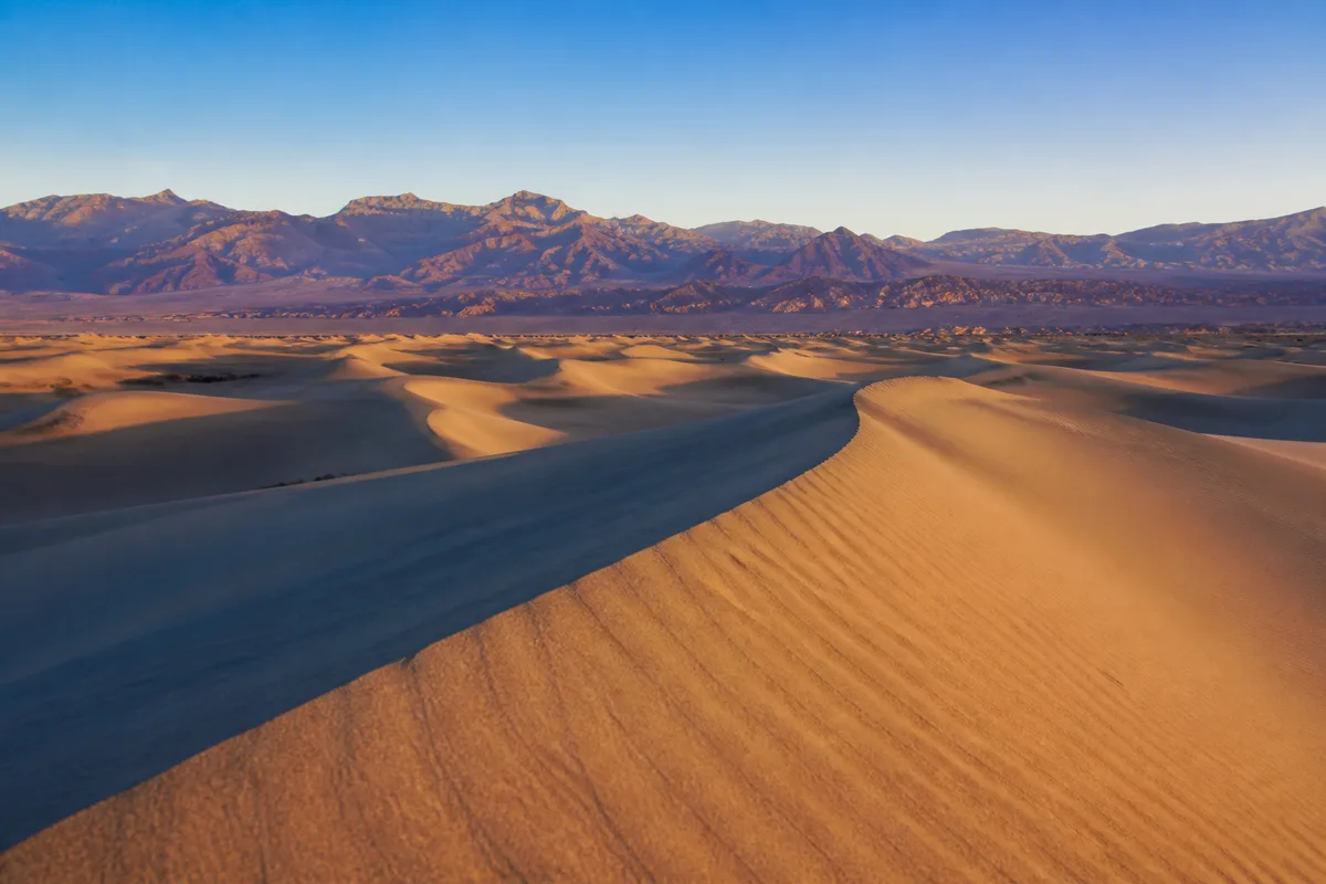 Dunes de sable et montagnes arides dans un désert au lever du soleil